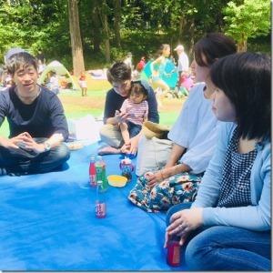 子供たちが駆け回る公園で女の子を膝に抱えた男性を含めた男女4人が話し合いをしている写真